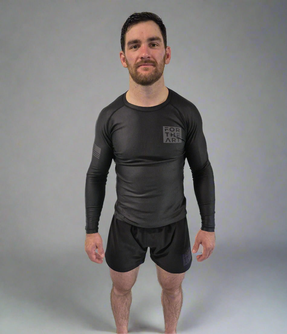 Man wearing a black long-sleeve athletic shirt and shorts against a white curtain background